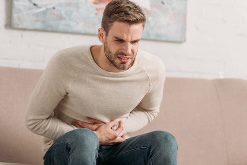 young-man-sitting-on-sofa-and-touching-stomach-whith-hands.jpg